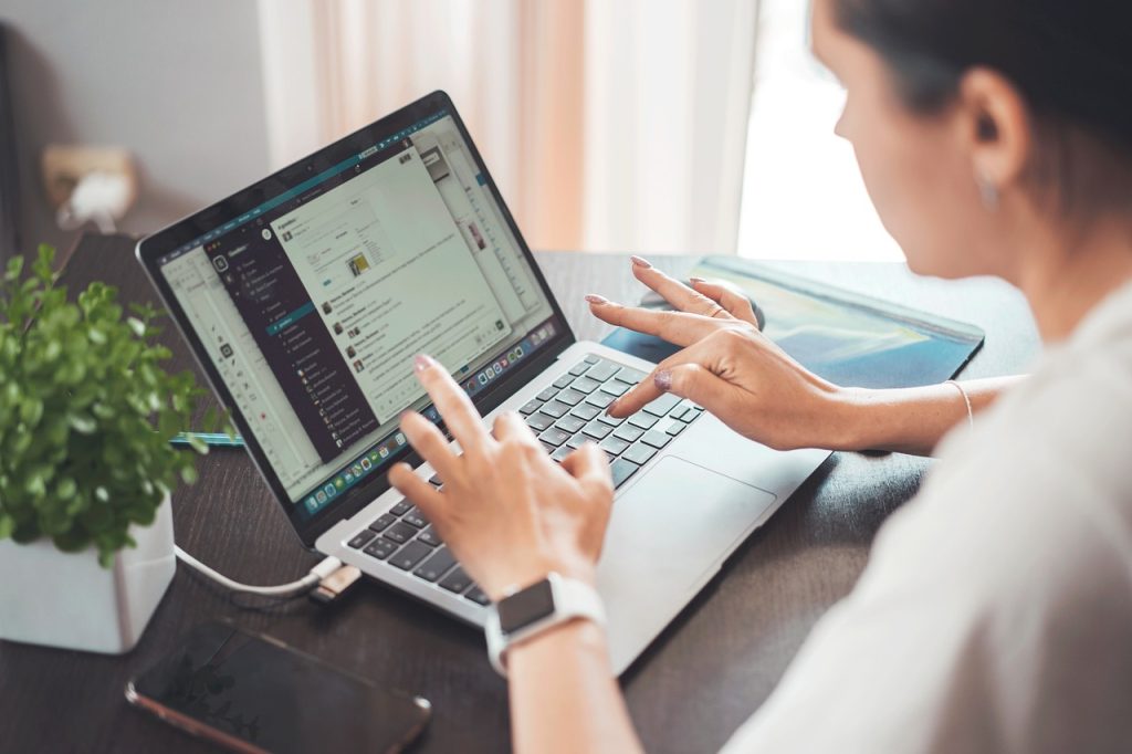 Person working on a laptop with an open chat application, mobile and plant on the desk for productive workspace